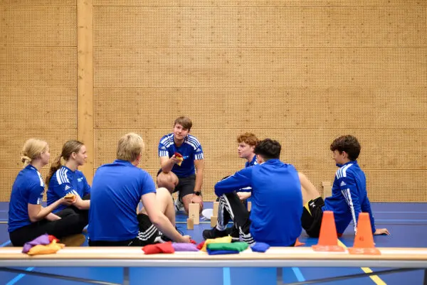 MBO-studenten in een sportzaal zittend op de grond luisterend naar instructie van de docent