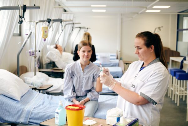MBO-studente Verpleegkunde met een docent in een praktijklokaal met ziekenhuisbedden