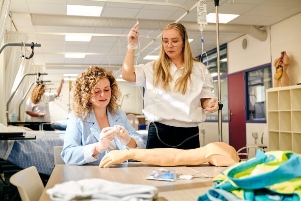 mbo-studenten zorg en welzijn oefenen met een infuus in te prikken in arm
